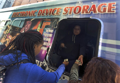 A New York-i Norman Thomas Gimnázium diákjai fizetnek egy dollárt, hogy ellenőrizzék elektronikus eszközeiket egy furgonban iskola előtt.