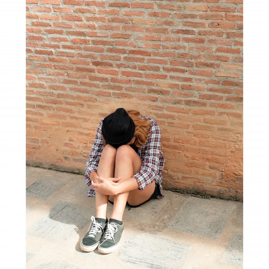 A student sits outside a school with her head down, looking upset.