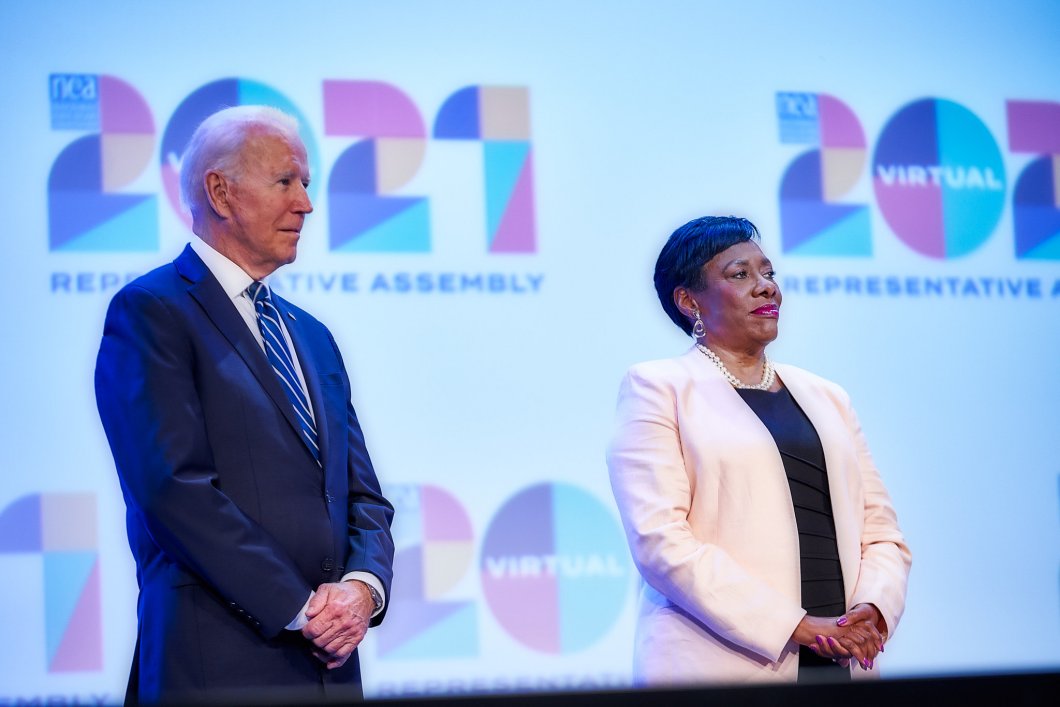 President Joe Biden and NEA President Becky Pringle stand next to each other in front of the 2021 NEA RA logo