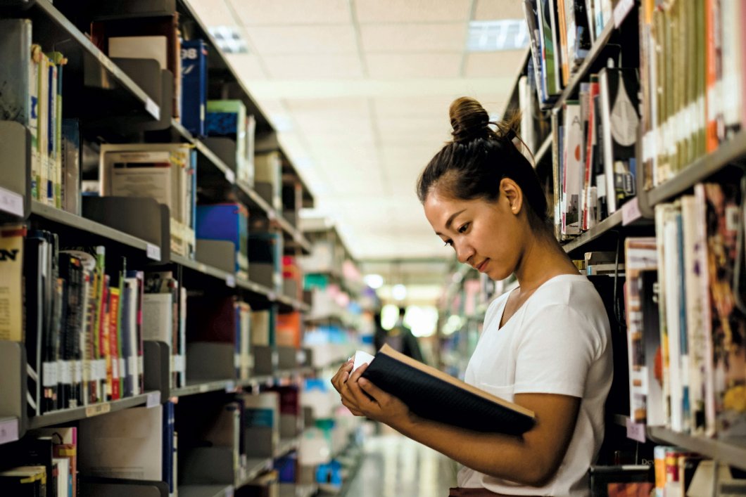 Asian girl reading a book in a library.