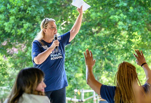 Woman speaking in front of group with a microphone and her hand raised