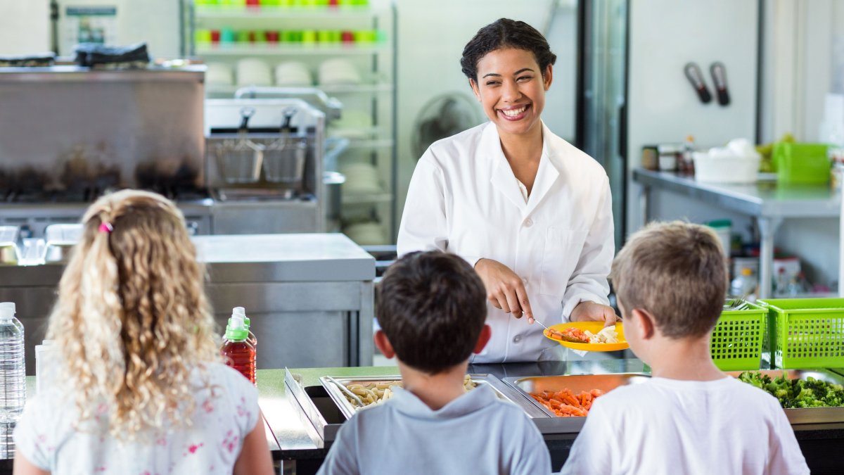 Woman serves three children food in a school cafeteria