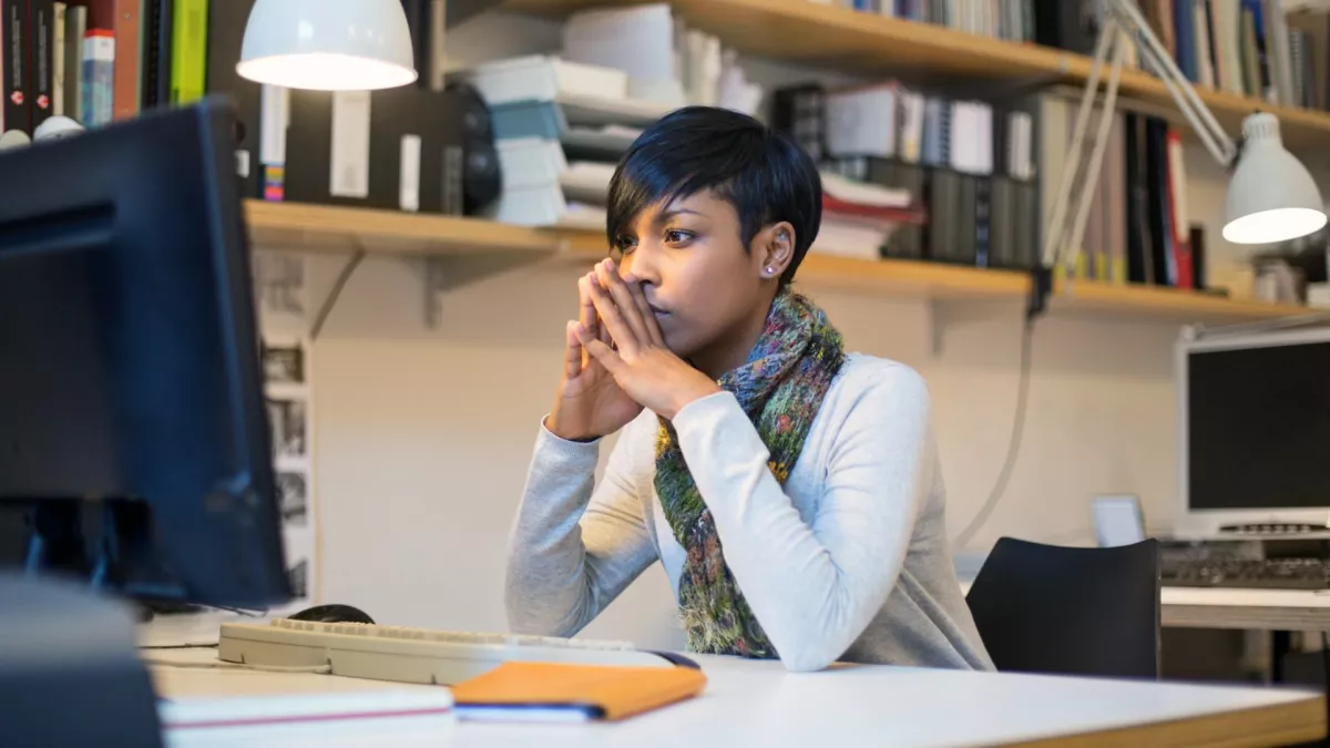 young female teacher sitting at desk and reading on a desktop computer