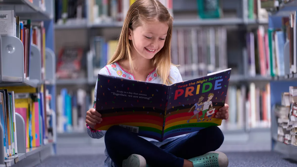 young girl in the library reading a copy of The Night Before Pride
