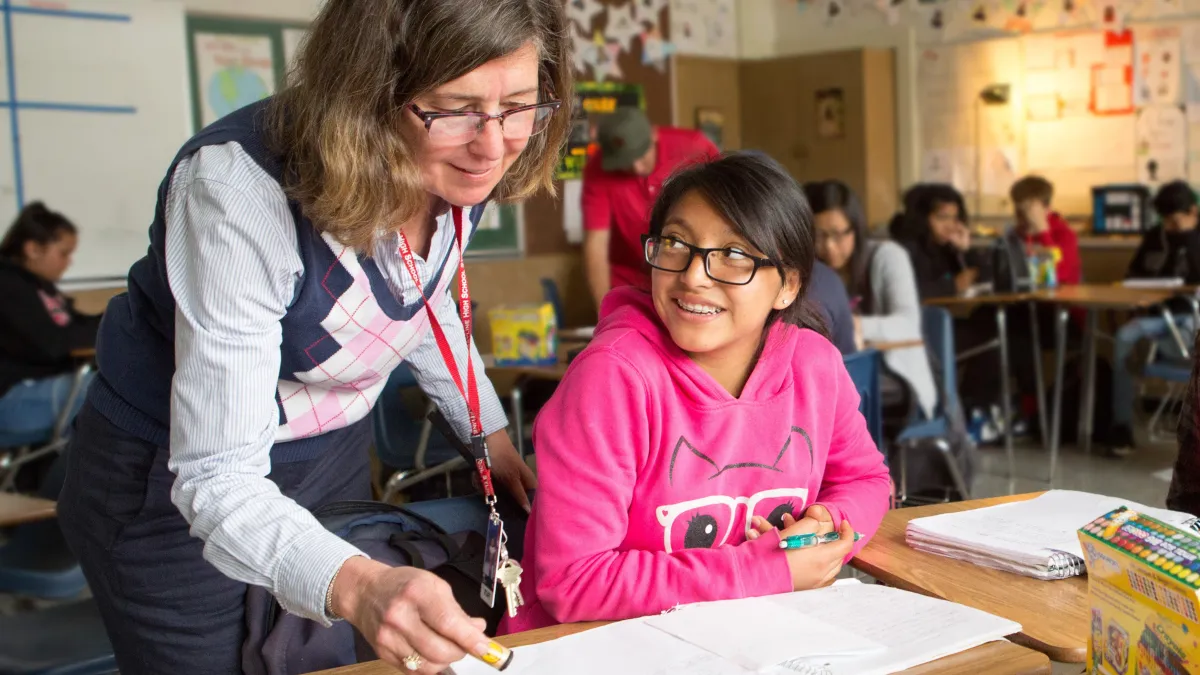 Smiling educator helps a student with her classwork. 