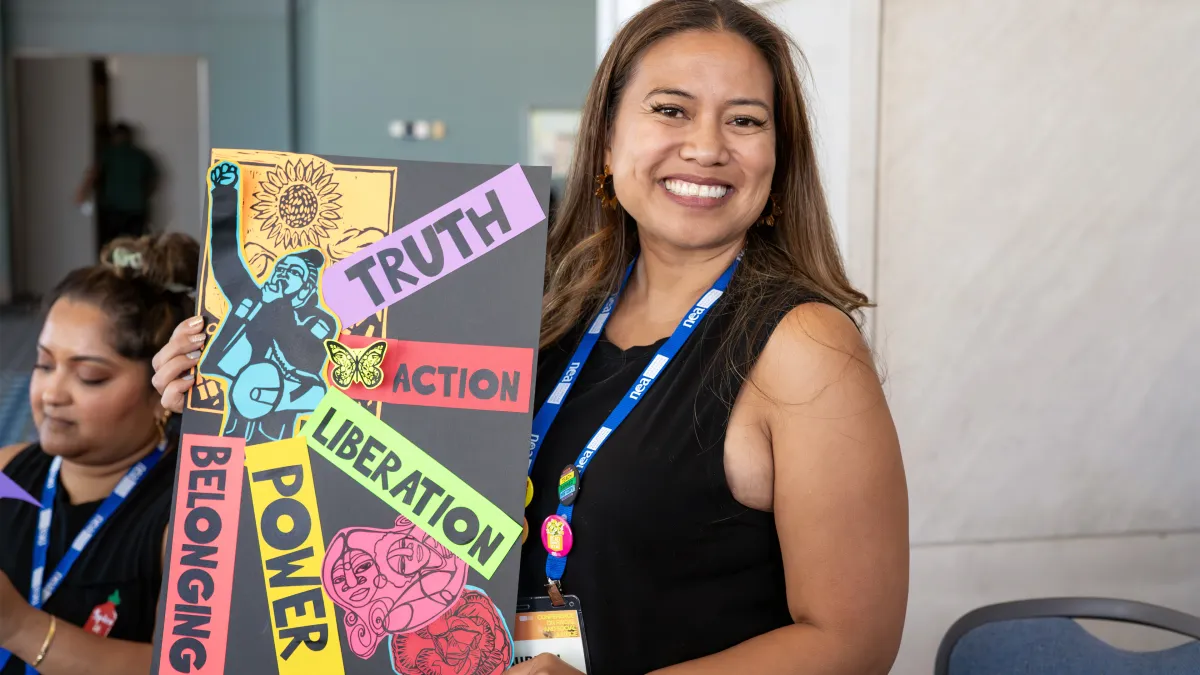 A woman at the 2024 NEA Conference for Racial and Social Justice holds up artwork with the words truth, liberation, power, and belonging