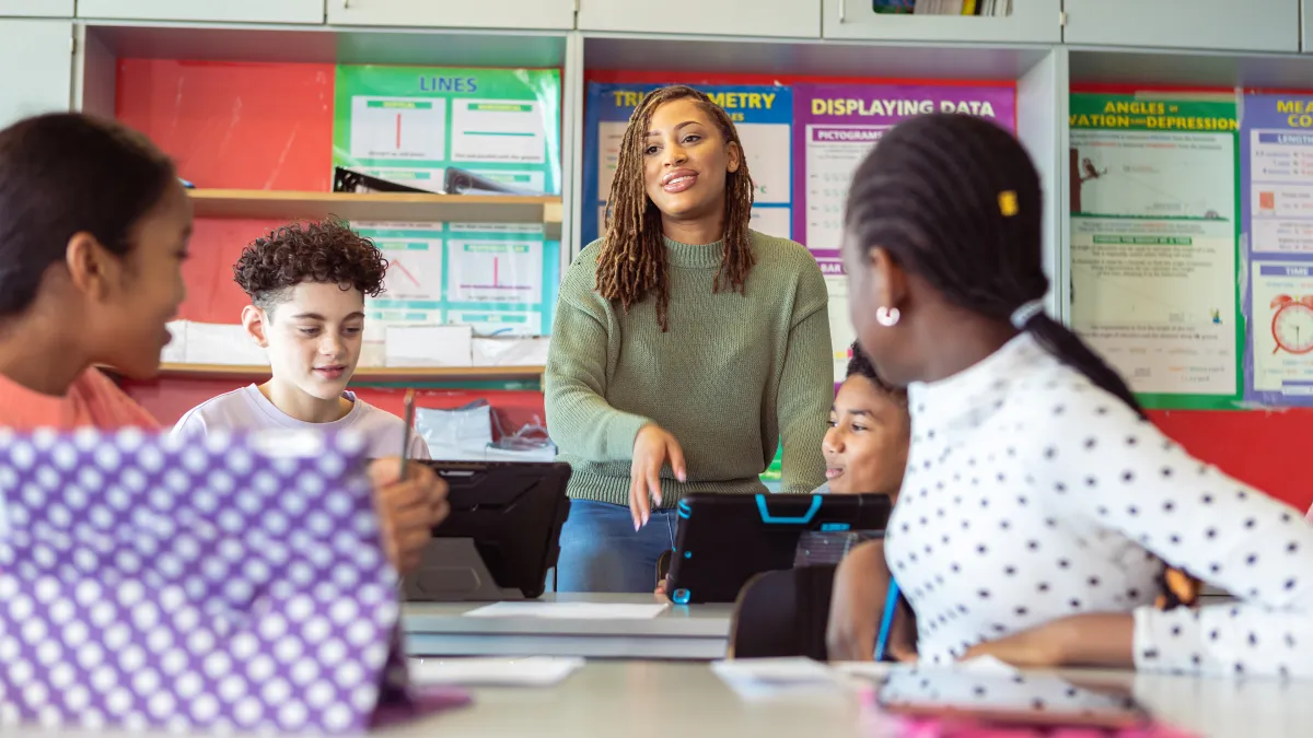 Black female teacher stands next to a table of students in the classroom during a discussion