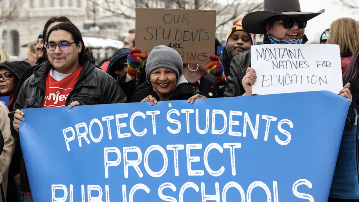 Educators rally at the US Capitol dressed in winter clothes. They carry a blue banner that says "Protect Students Protect Public Schools"