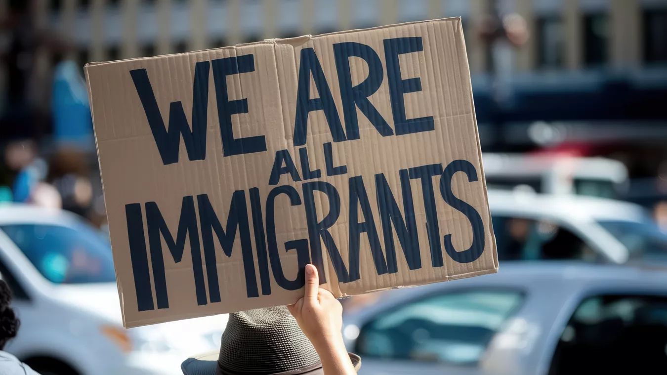 Hand holding a sign that reads, "We are all immigrants."