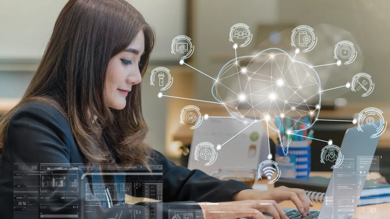 A woman working on a laptop displaying a brain shape surrounded by artificial intelligence icons.