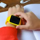 student adjusts a bright yellow smartwatch on his wrist in school