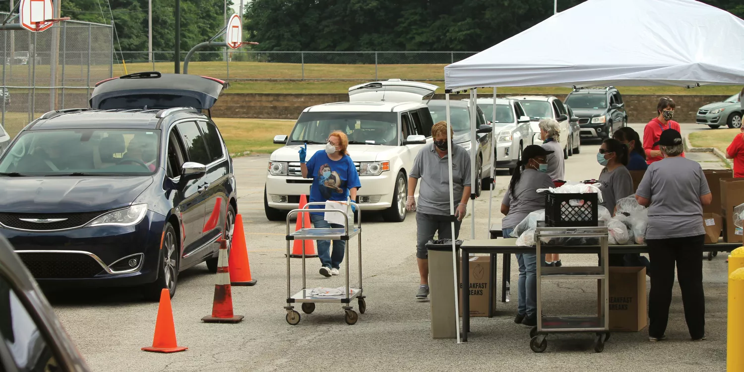Doriann Wiegand wears a mask as she distributes food to cars lined up with their trunks open.