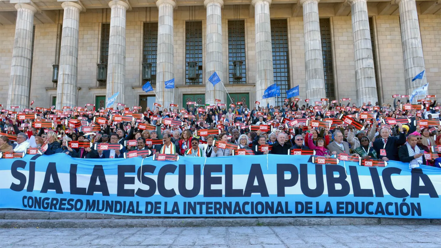Attendees the 10th EI World Congress stand behind a banner that reads Si a la Escuela Publica