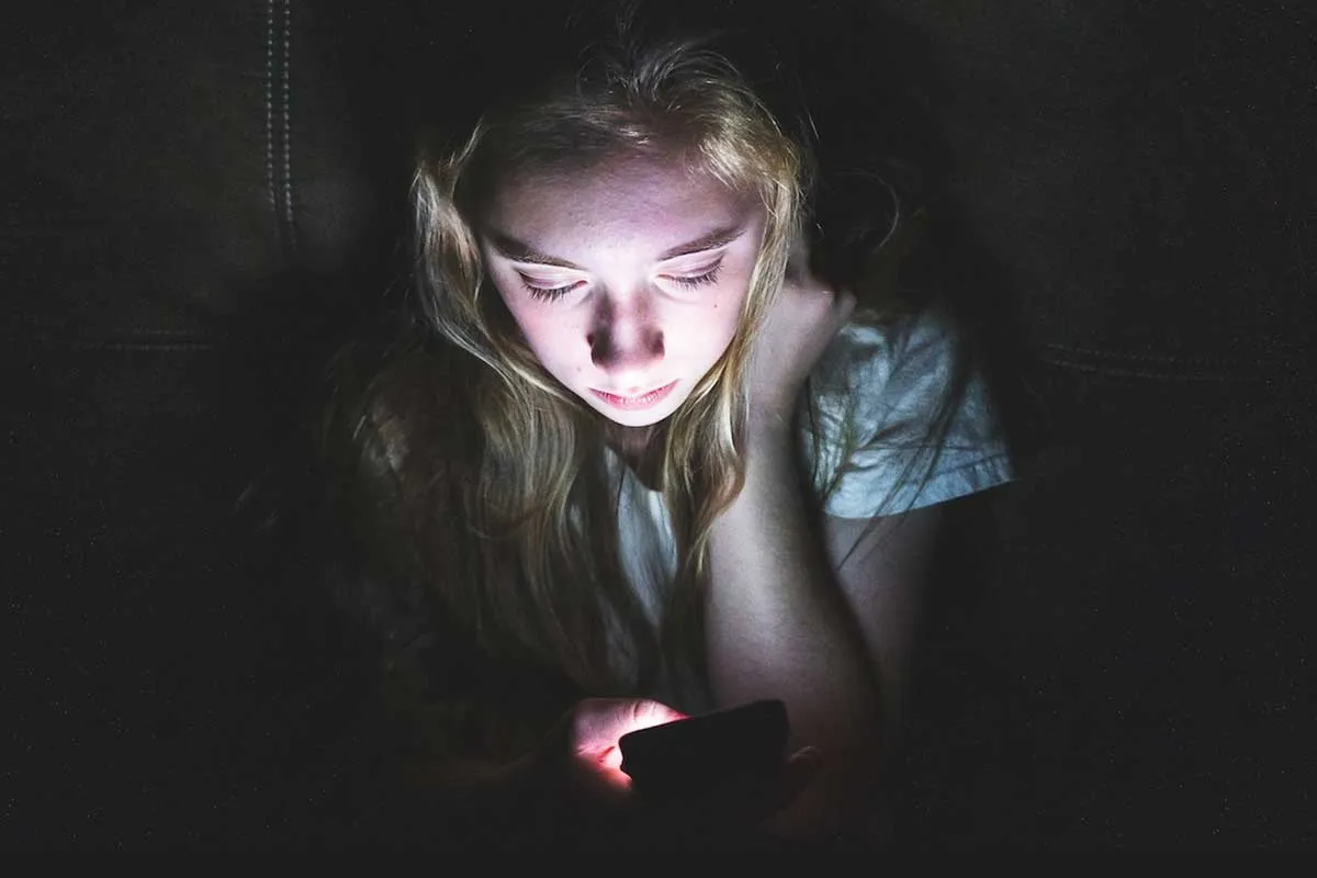 Young white female looking at her mobile device in the dark.