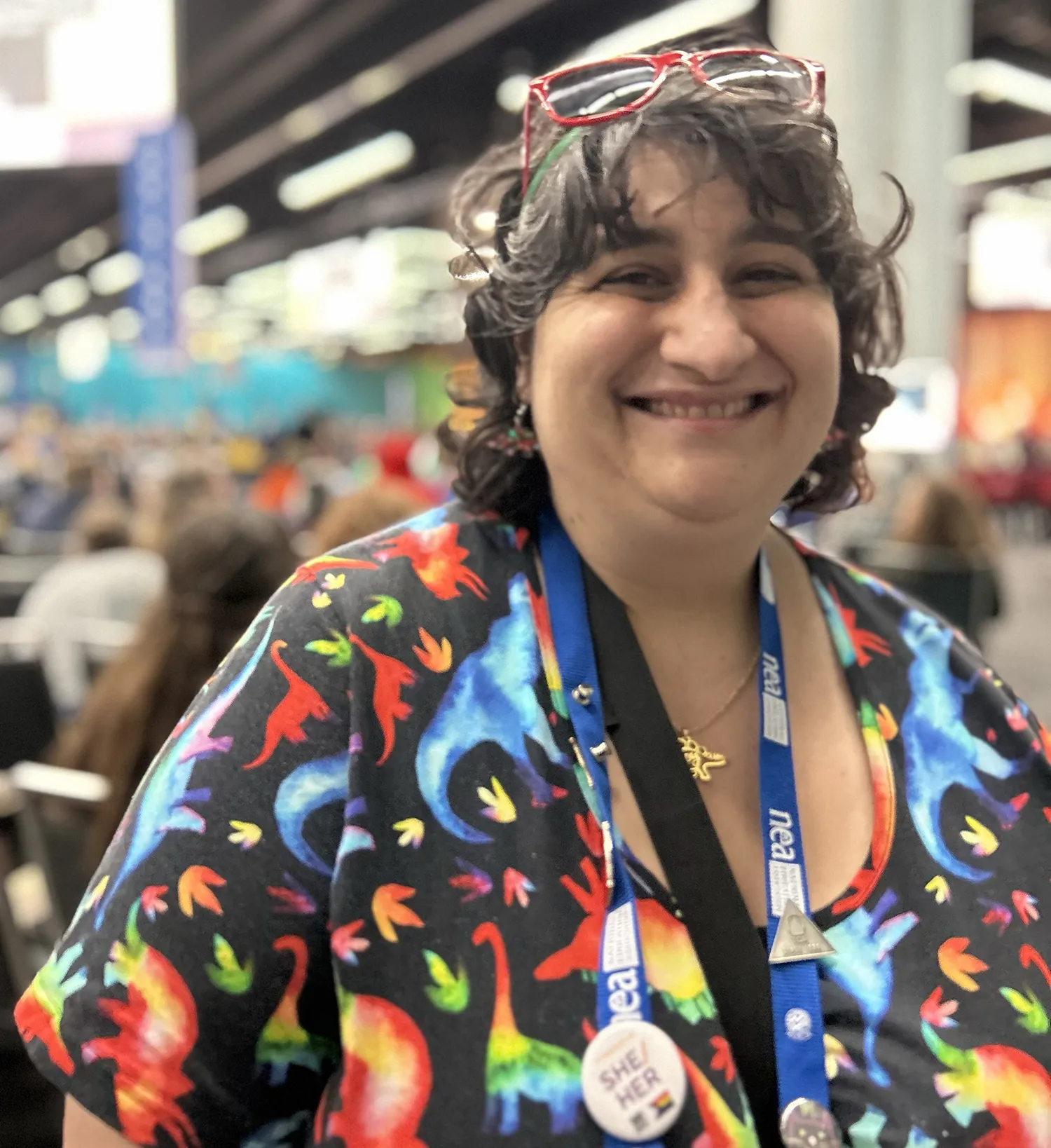 A cheerful woman wearing glasses and a vibrant shirt smiles warmly at the camera.