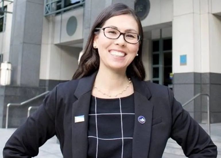 A woman in a black suit and wearing glasses smiles confidently.