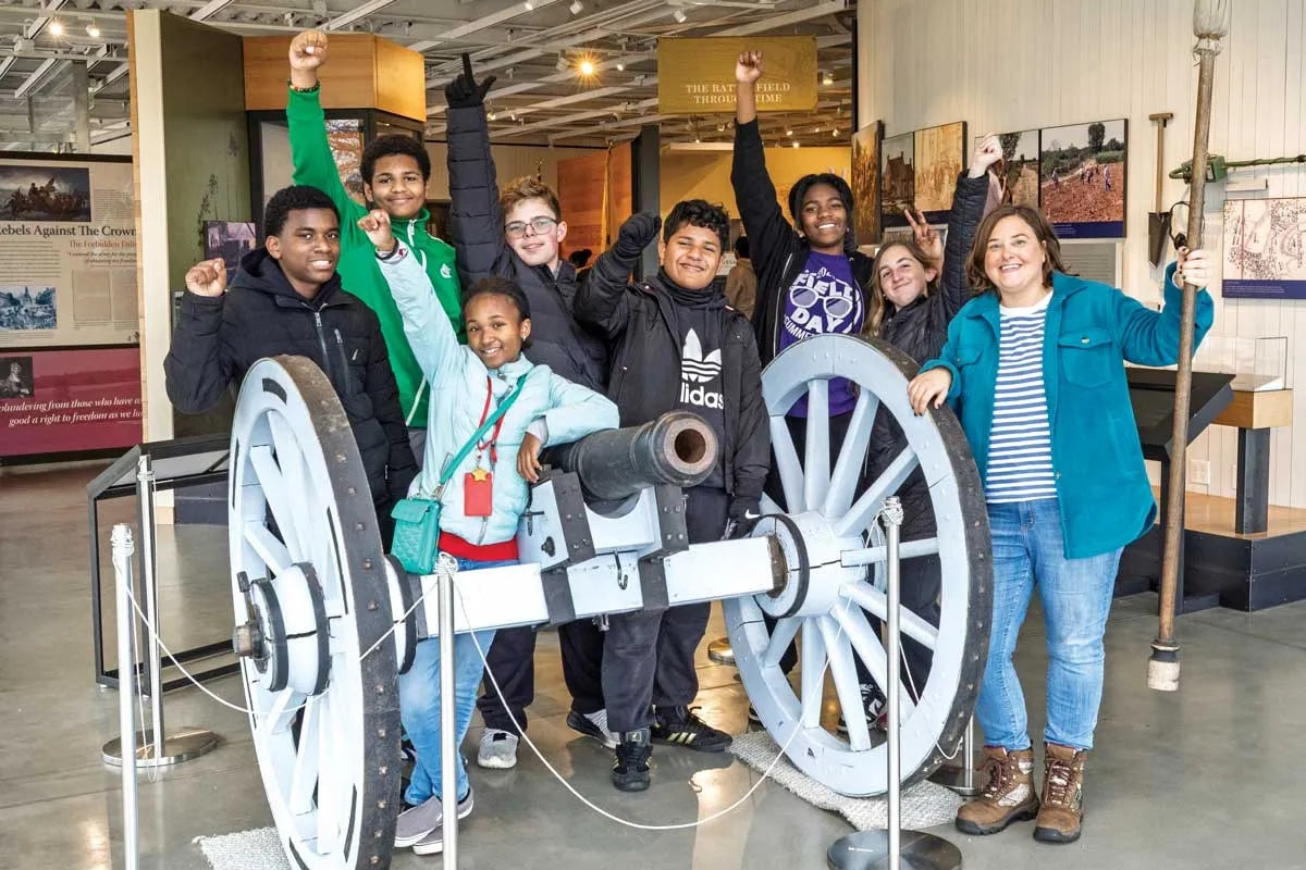Laura Ellis with her students raising their fist in the air while standing behind an historic canon.
