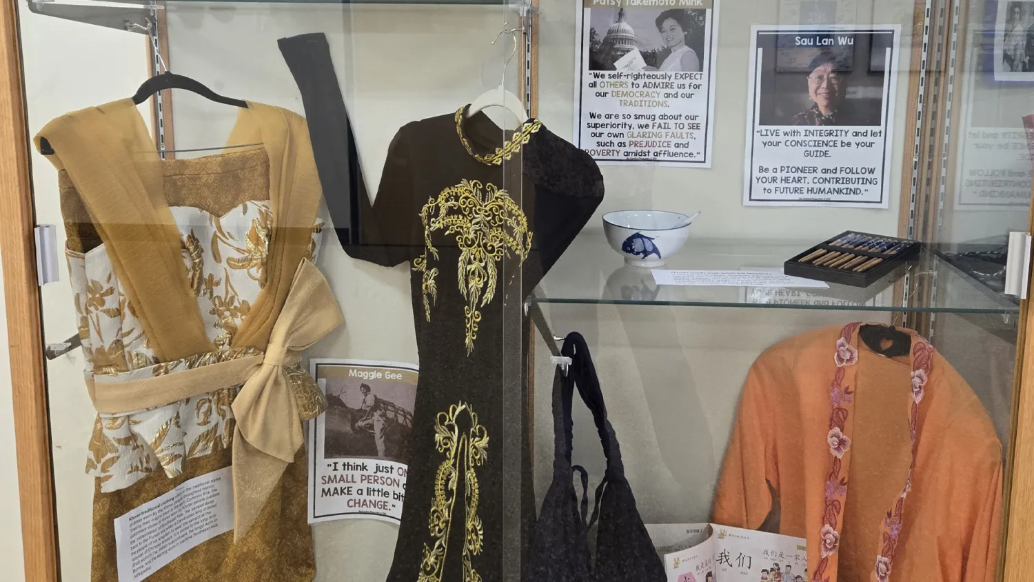 A display case with a traditional Asian attire, surrounded with photographs of historic people of Asian descent. 