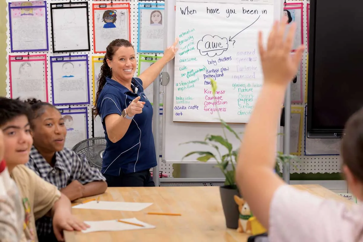 Debi Lawson in the front of her classroom pointing to a student raising his hand.