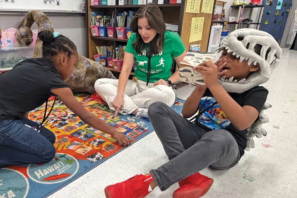 Megan Donoghue sitting on the floor with students playing with dinosaur games.