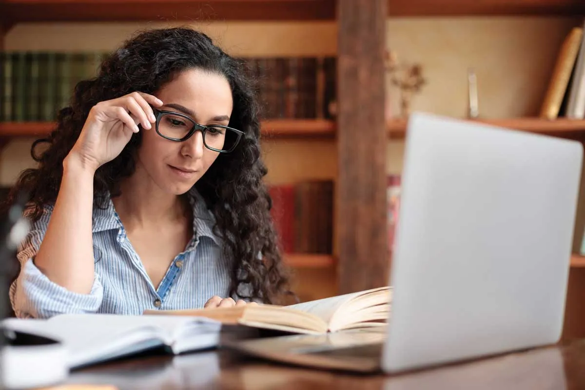 Female educator reading a book on top of a laptop.