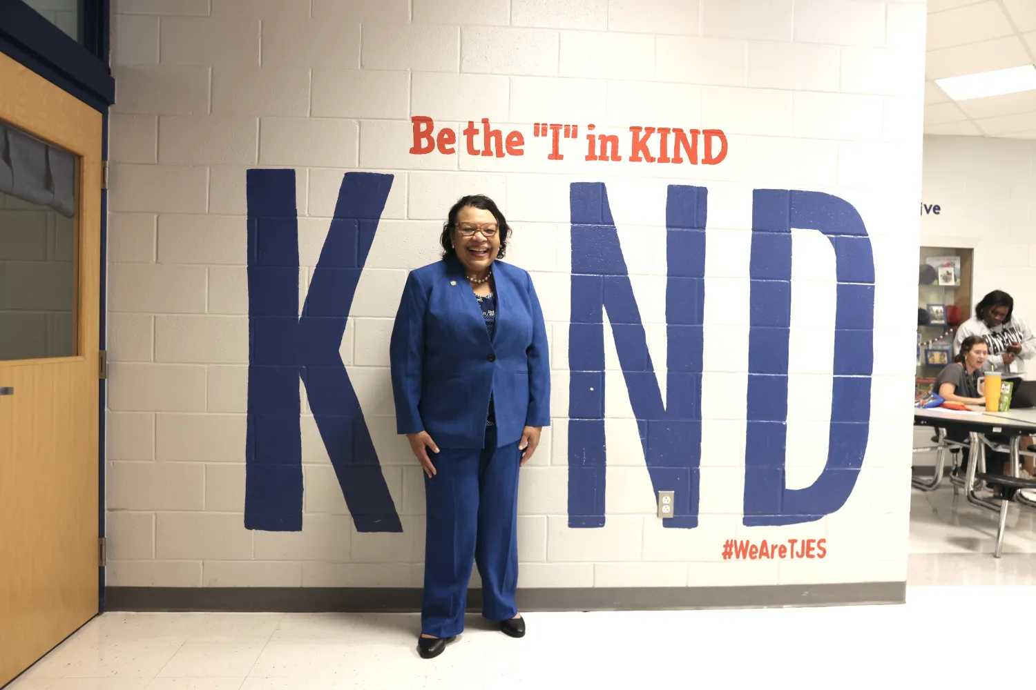 Princess Moss standing in the Be the I in Kind wall sign