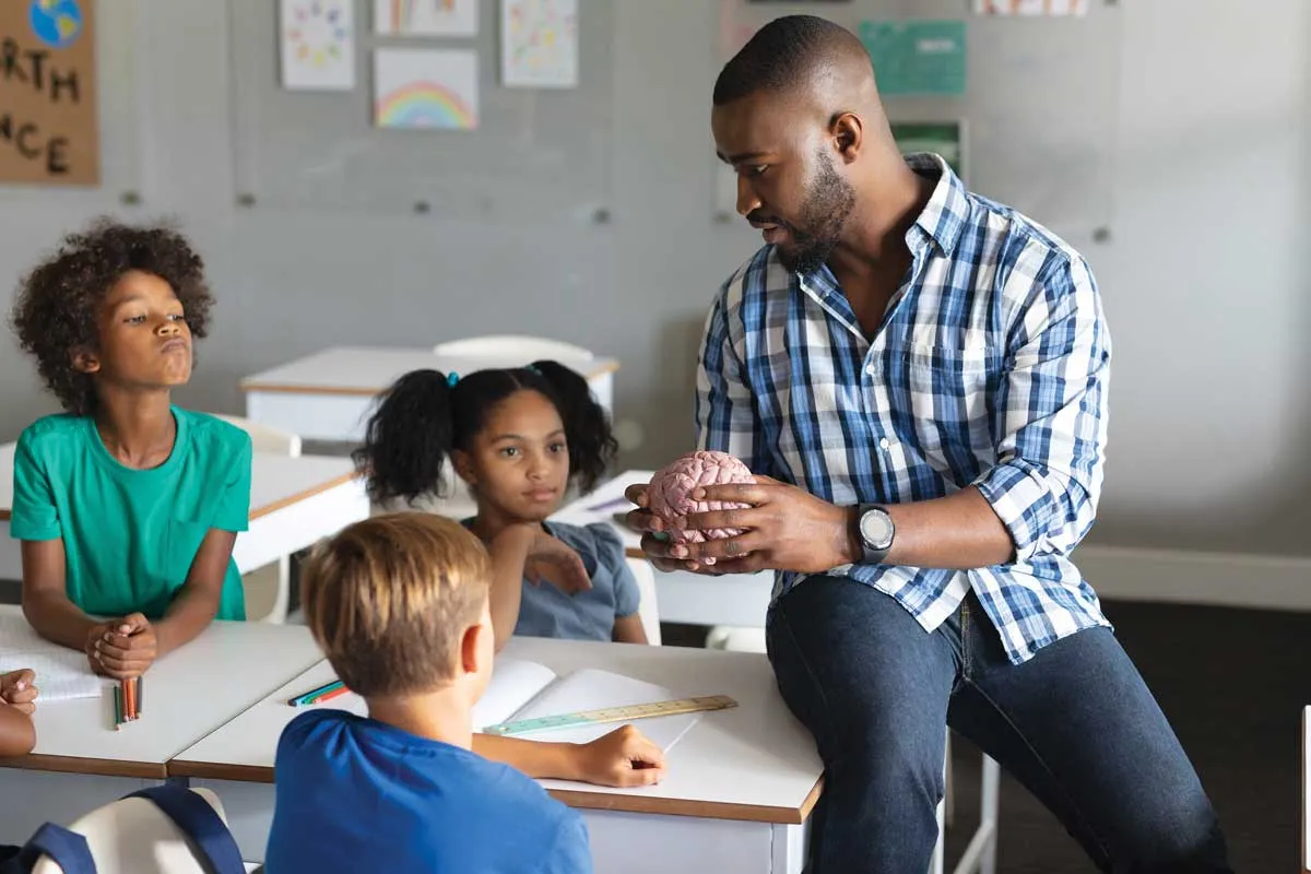 Black male teacher talking to a small group of diverse students.