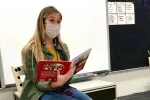 Stephanie Duwve, wearing a PPE mask, sitting at the front of her classroom reading to her students.