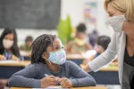 masked female student with masked teacher in classroom