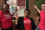 NCEA President Tamika Kelly, NCAE Vice-President Bryan Proffitt, and NEA President Becky Pringle point to NCAE signs in a storefront.