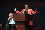 Becky Pringle speaks at a town hall while Senator Bernie Sanders sits on stage and listens