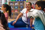 Teacher Michelle Cardenas sits on a rug in her classroom with students