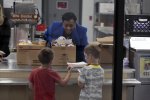 NEA President Becky Pringle hands out food to 2 young students in an elementary school cafeteria