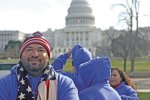Jorge Botella stands outside in Washington DC with an American flag scarf and hat and the US capitol building in the background