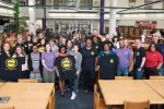 Becky Pringle stands in a library with a large group of Fairfax educators holding up black and gold FEU t-shirts