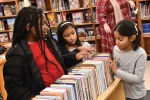 Black female educators helping two young female students of color at a library
