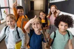 6 elementary students walk down a school hallway with thumbs up looking at the camera