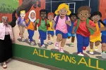 Retiree Joni Richman Watson in front of a student mural with words that say All Means All