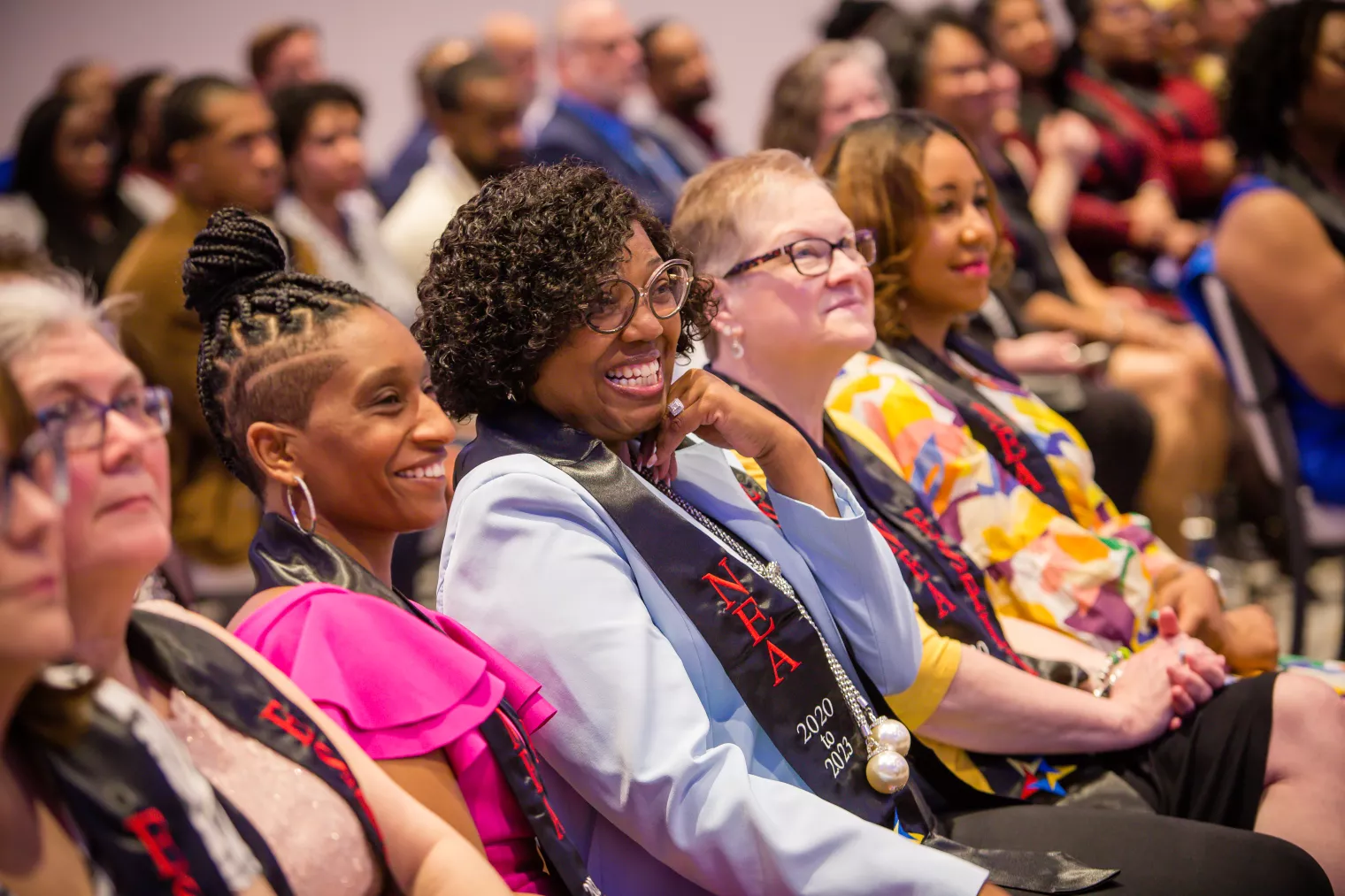 A group of education support professionals sit in an sudience, smiling