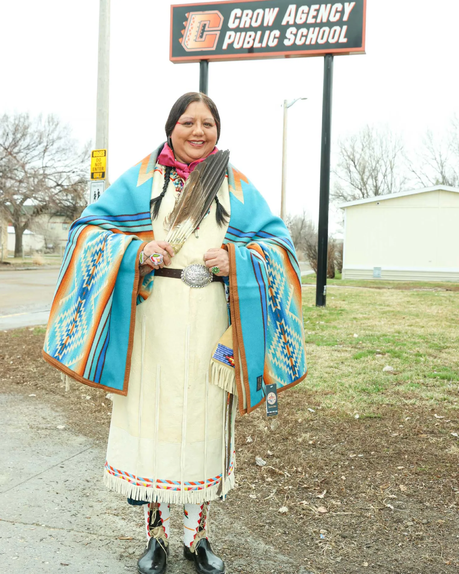 Lucy Real Bird outside the school with the Crow Agency Public School sign.
