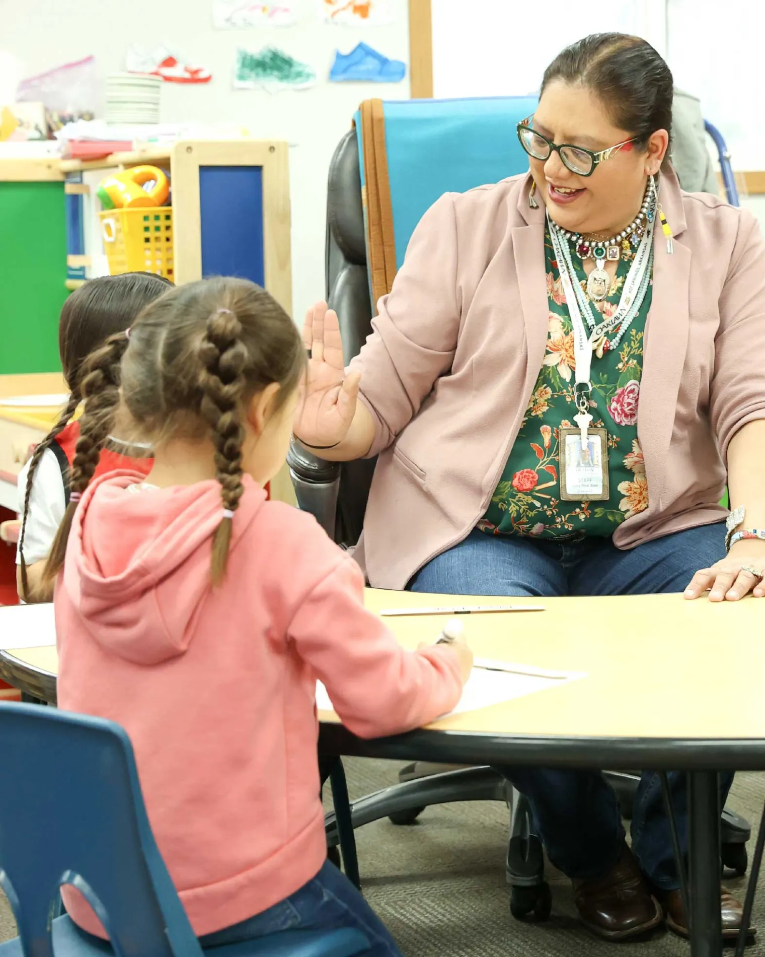 Lucy Real Bird sitting at a table with students offering one a high-five.