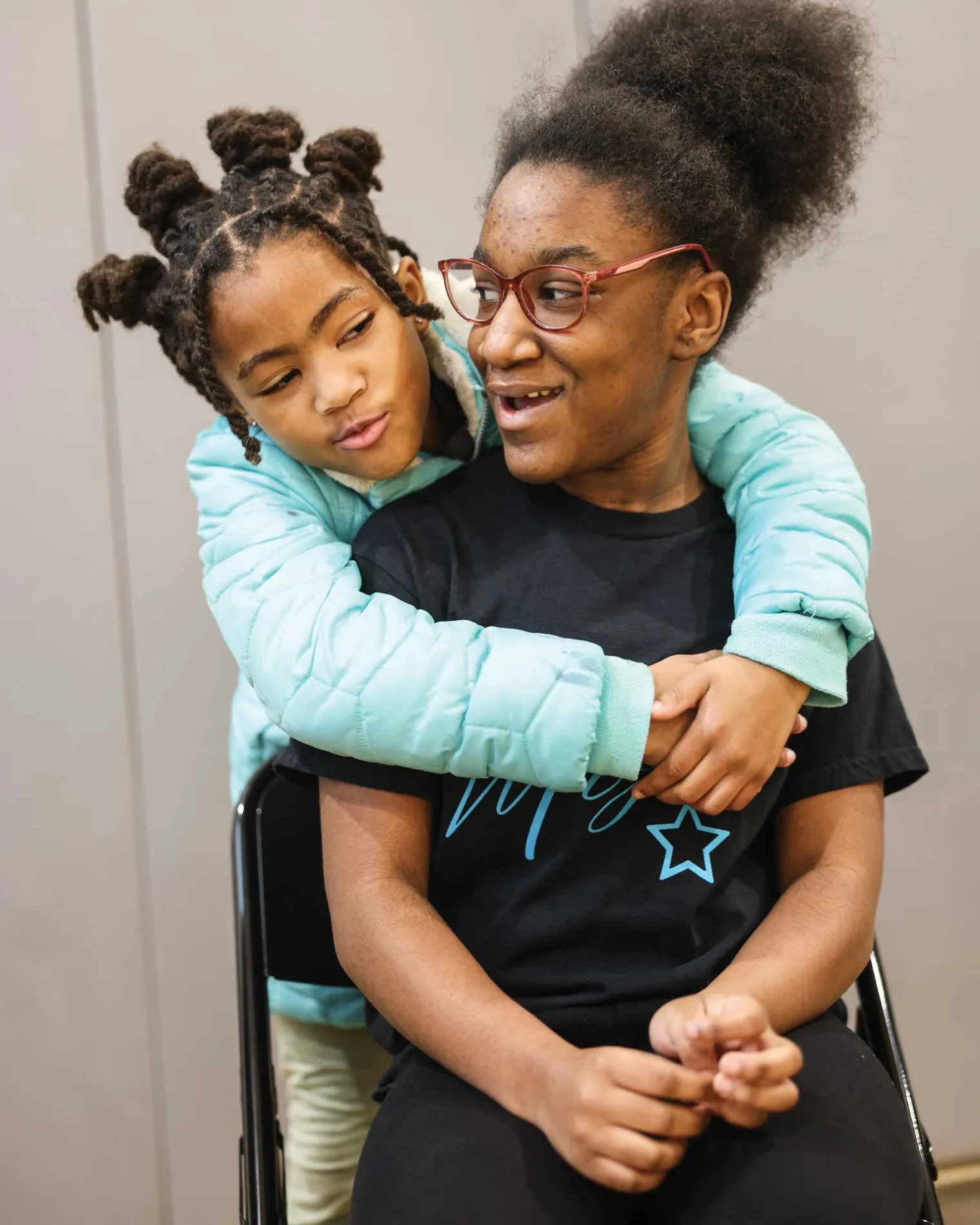 Two female IDEA students with one hugging the other from behind.
