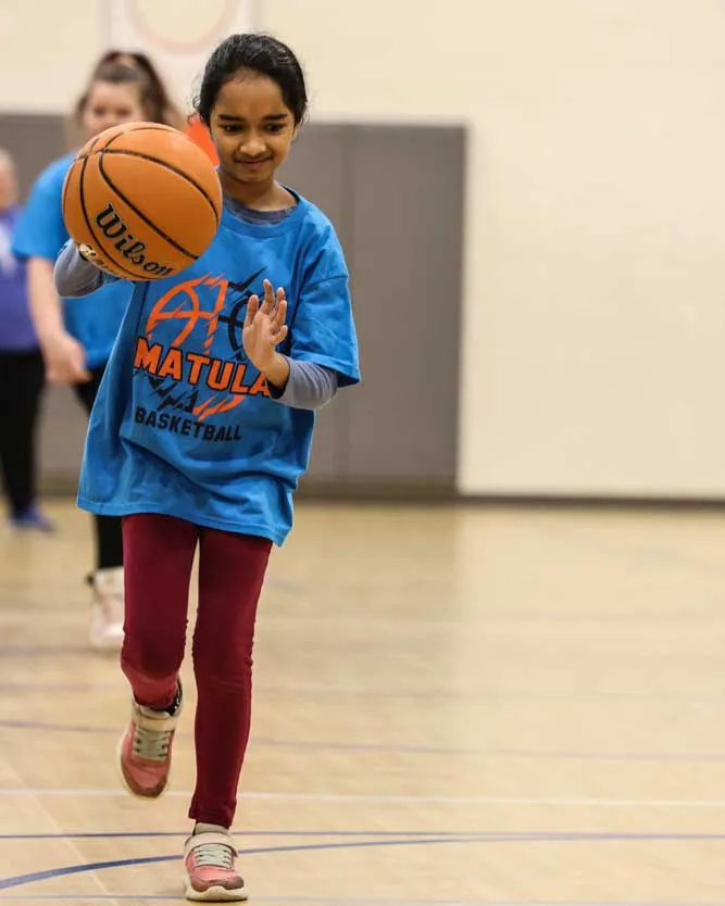 Female student dribbling a basketball down the court.