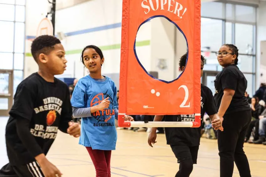 IDEA students around a vertical banner with a hole to shoot a ball through.