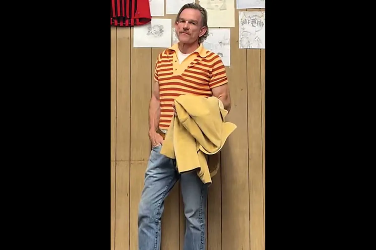 Mr. Ward, in a red and white striped shirt and jeans, holding a yellow jacket.