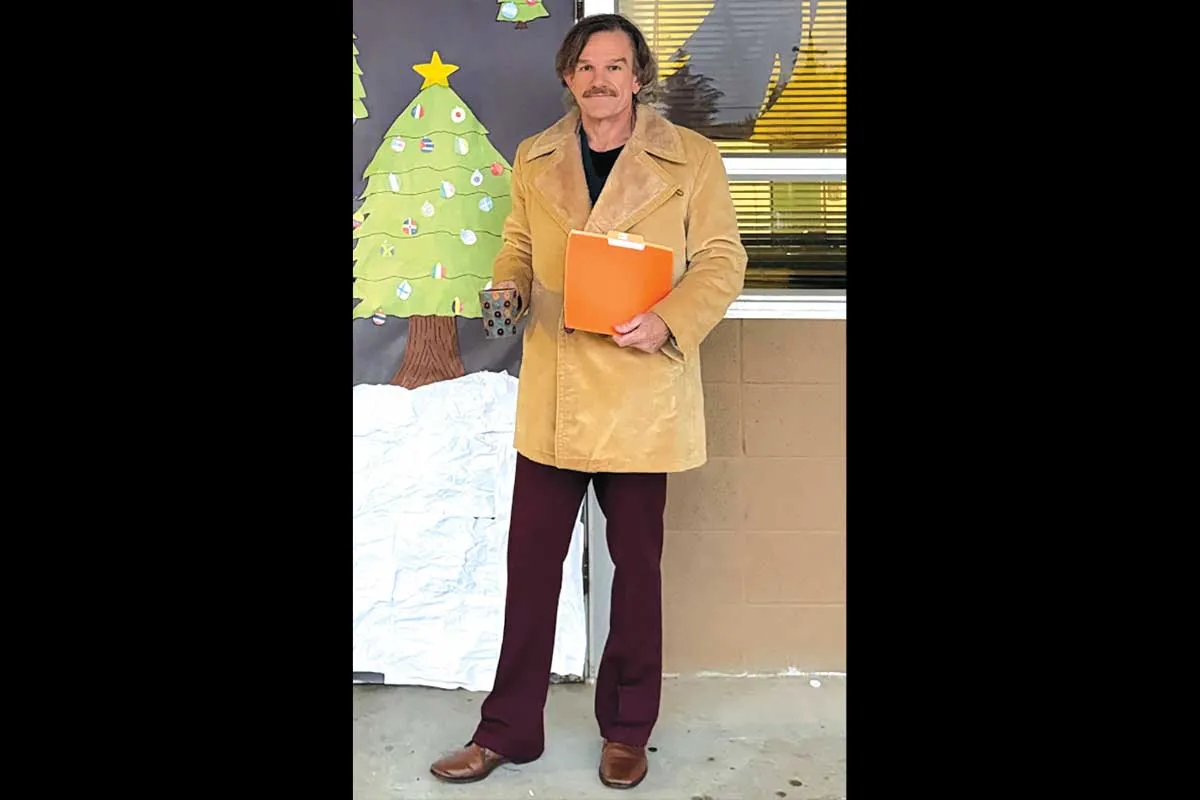 Mr. Ward wearing a beige overcoat standing in front of a door with Christmas decorations.