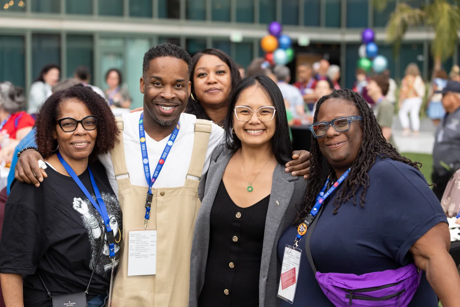 Five educators of color smiling at an outdoor reception with balloon decor in the background
