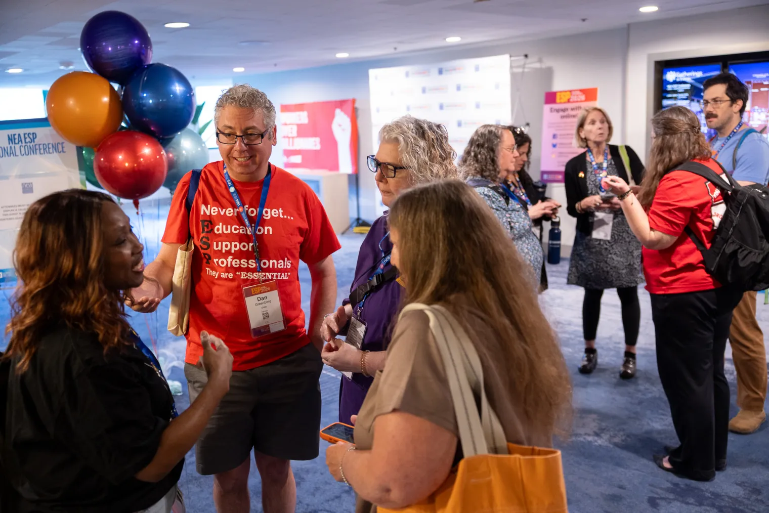 a group of educators chatting in a circle with a bundle of colorful red, orange, purple, and blue balloons in the back.