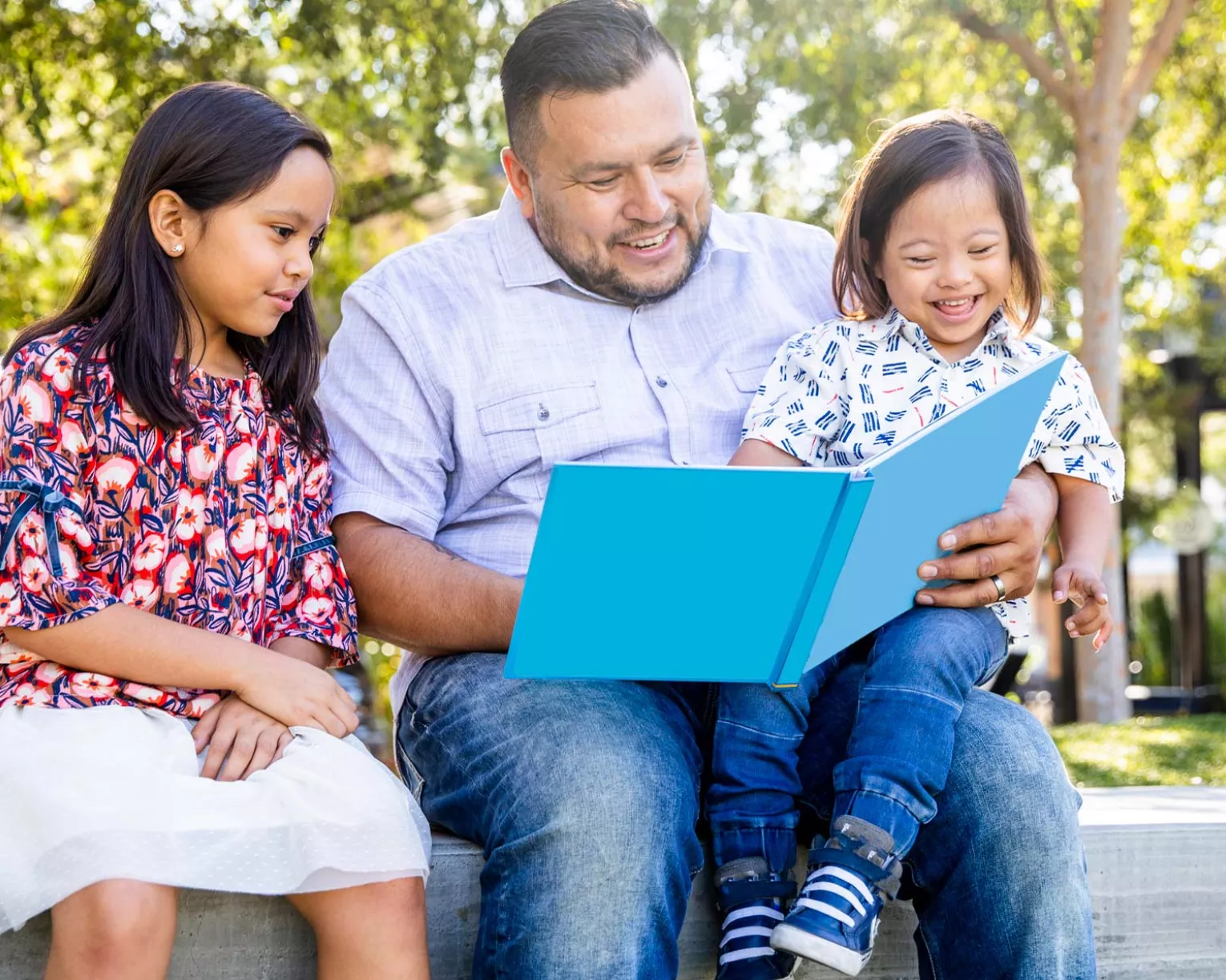 A father reads to his two daughters outside