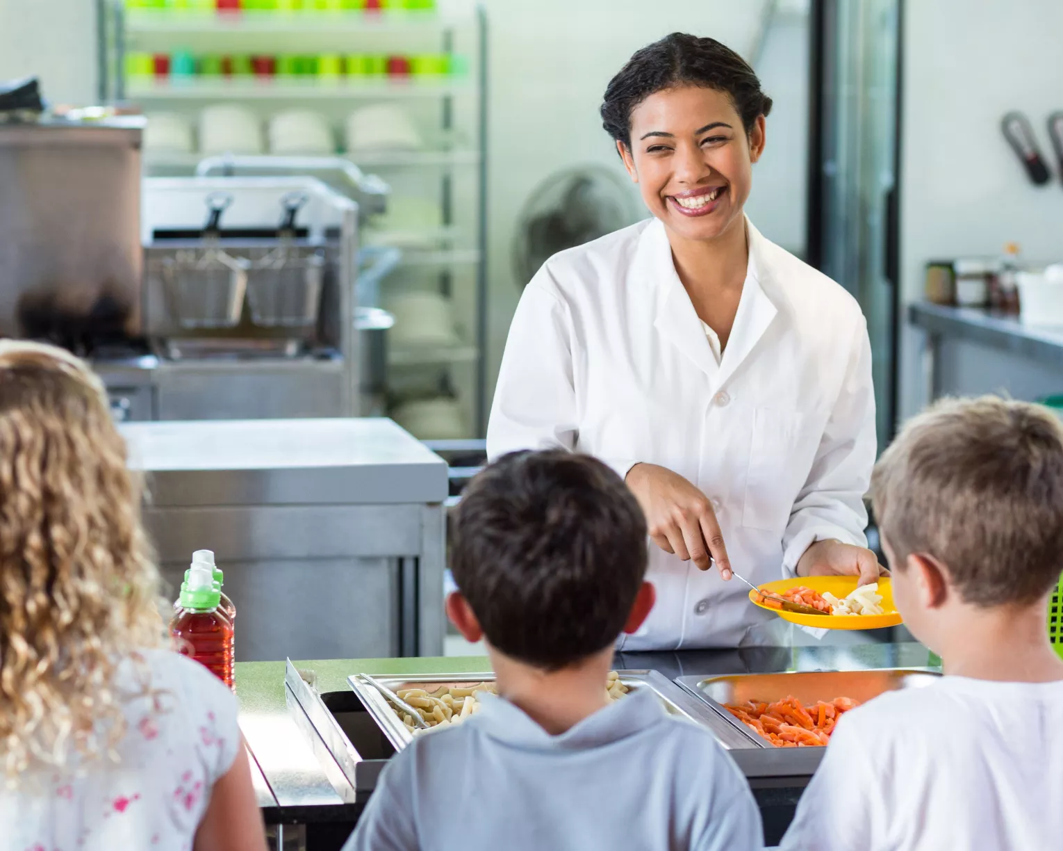 Woman serves three children food in a school cafeteria